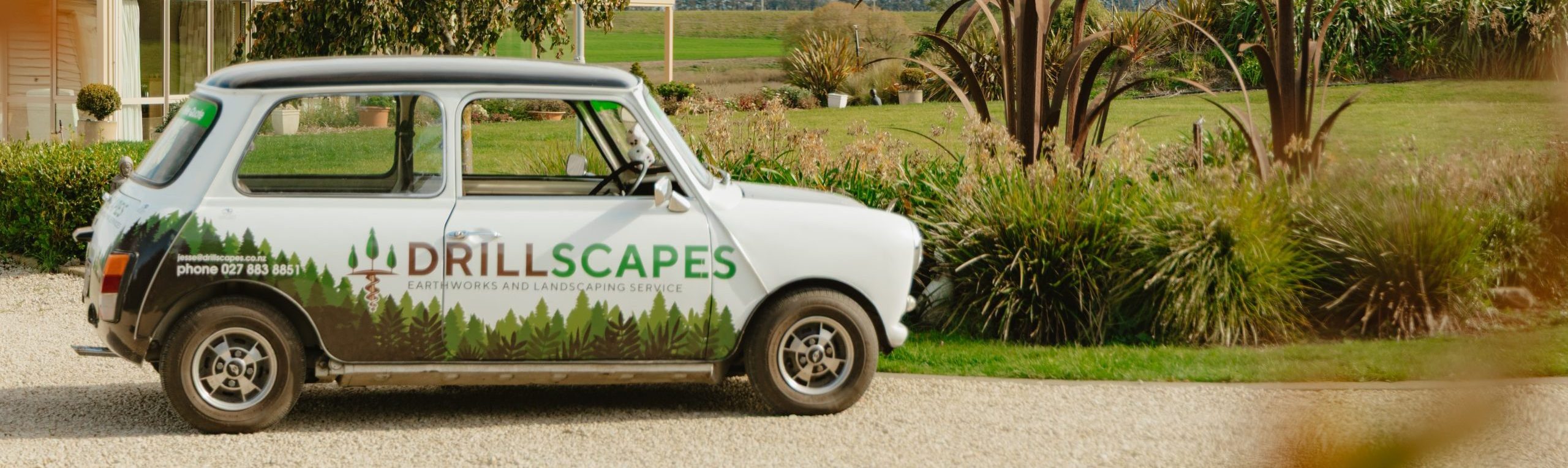 Branded Drillscapes Mini car parked on a grassy field with North Canterbury mountains in the distance.